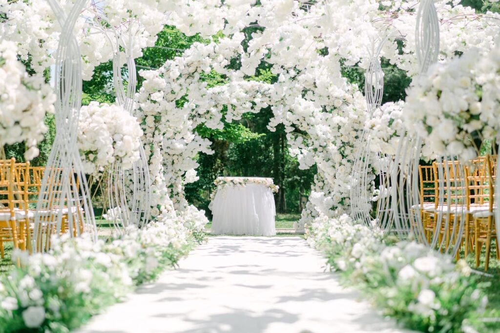 An elegant outdoor wedding venue setup with white floral arches and chairs.